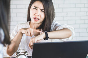 angry female boss pointing at her watch complaining her employee at workplace